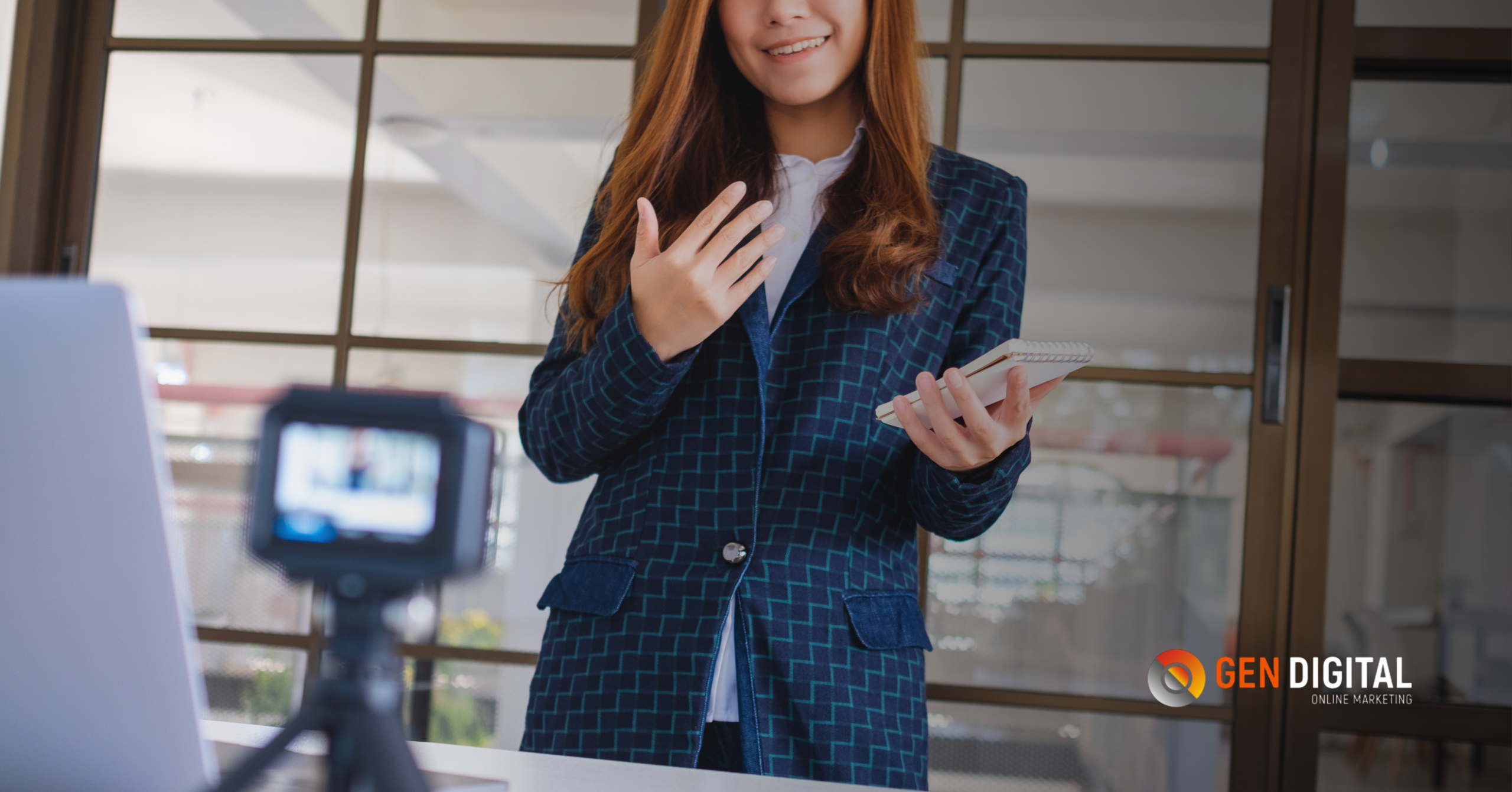 Mujer profesional grabando contenido para redes sociales desde una oficina, usando cámara y libreta de notas.
